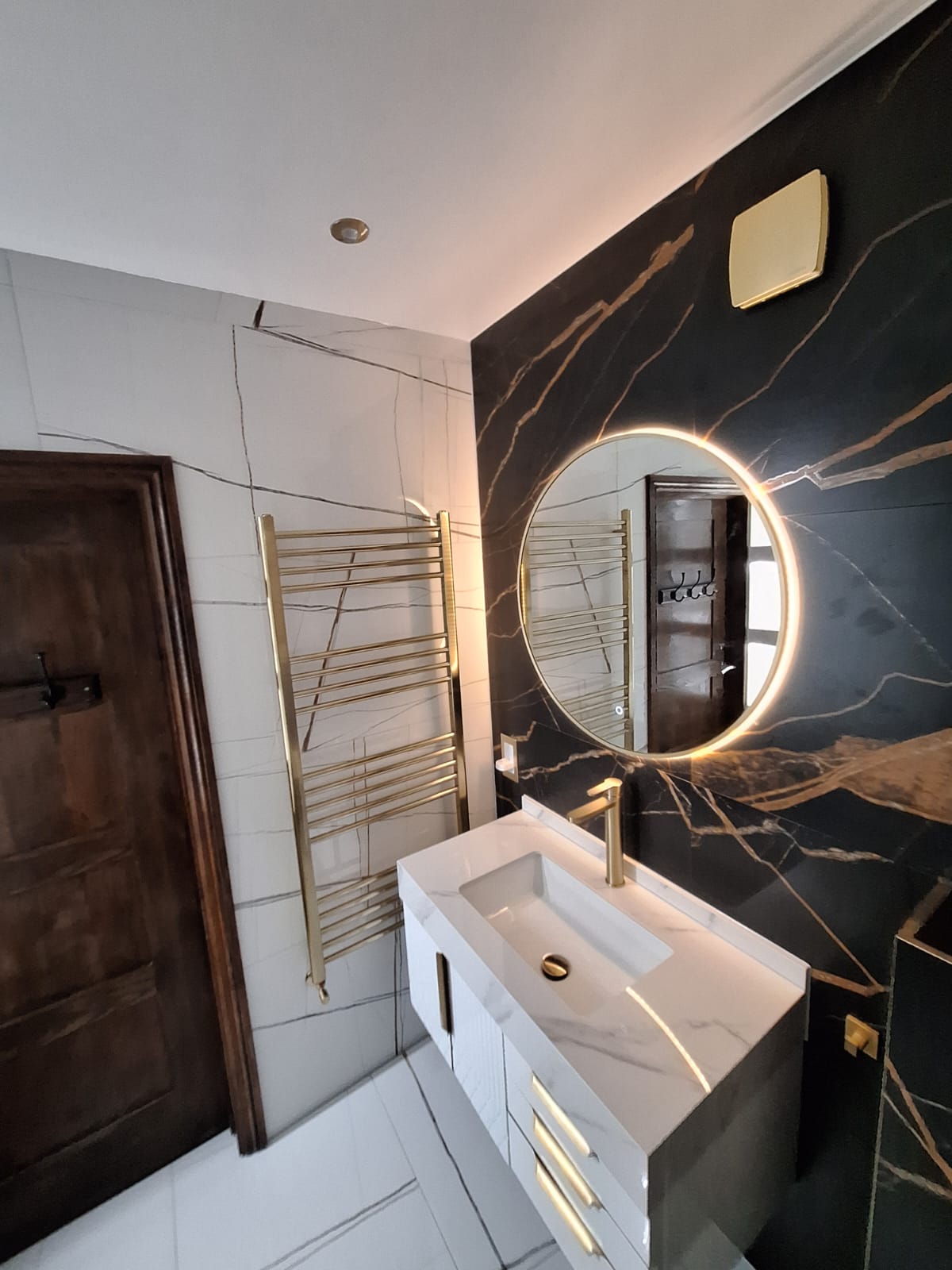 Backlit round mirror, brushed brass towel radiator and vanity reflection