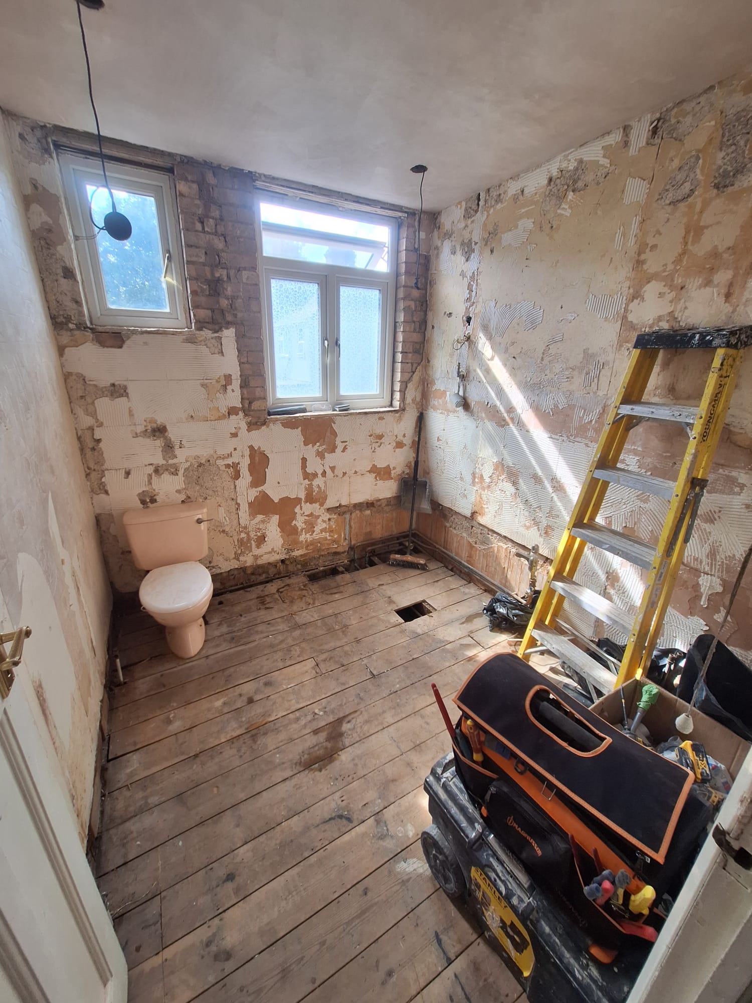 Before renovation, stripped bathroom with ladder, tools and exposed floorboards